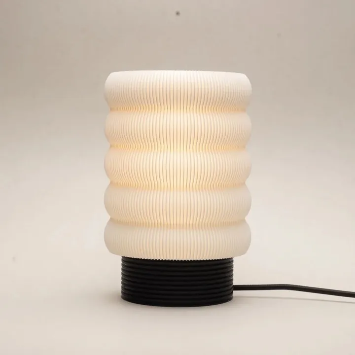 A white table lamp with stacked rounded rings on a black ribbed base, lit