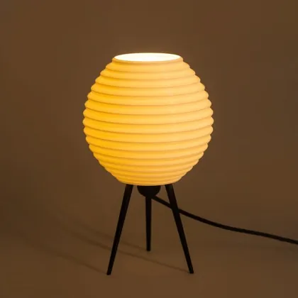A ridged tripod lamp, lit, on a brown backdrop